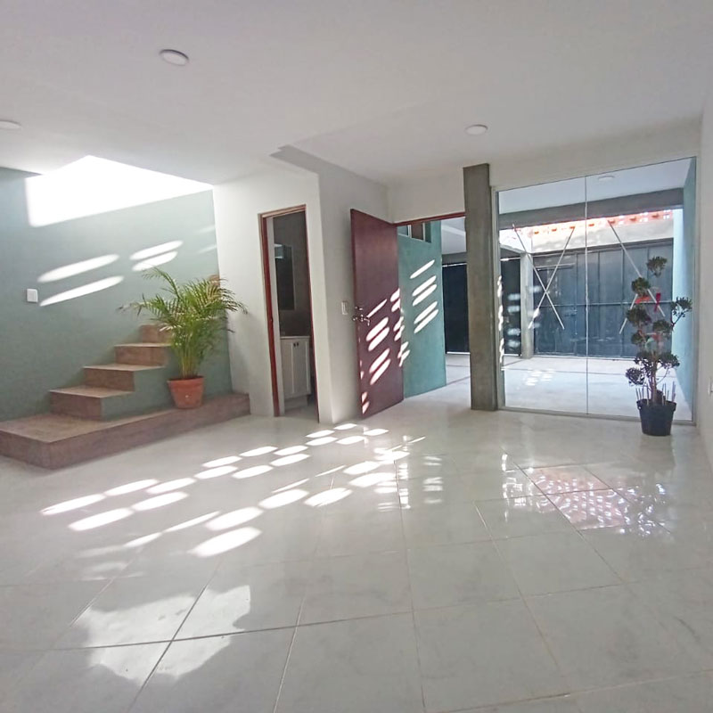 Interior of living room and front door with big glass window and lots of natural light, open space, and stairs to the second floor in private property home house for sale in San Agustín Yatareni neighborhood Oaxaca, Mexico