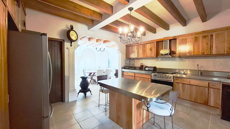 Stainless steel kitchen island with wooden cabinetry and beam ceiling — luxury Oaxaca real estate
