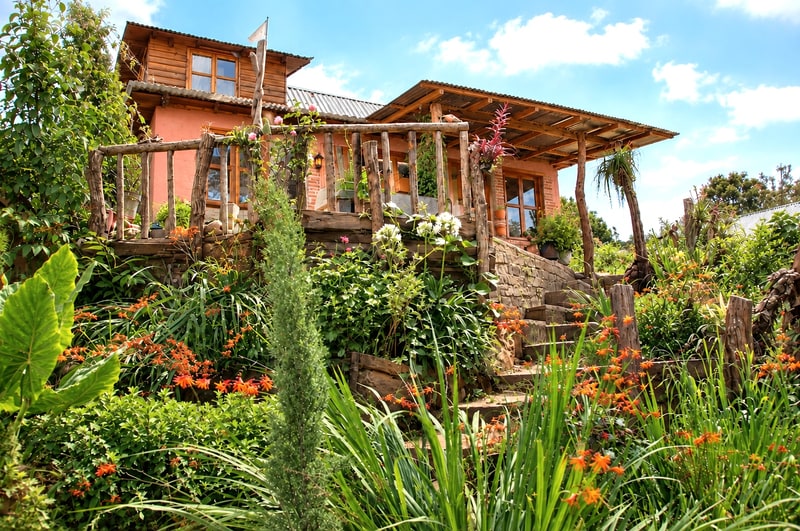 Guest house exterior with pole railing and flowering garden on the sloped lot, second dwelling on a titled property for sale near San José del Pacífico