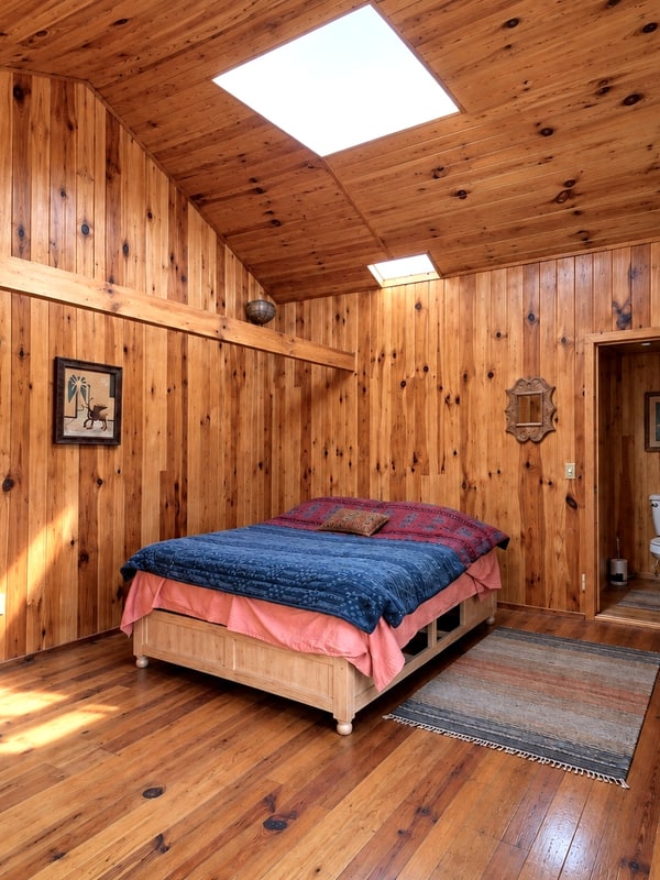 Master bedroom with wood plank walls and pitched timber ceiling in the main house of a furnished mountain home for sale near San José del Pacífico, Oaxaca