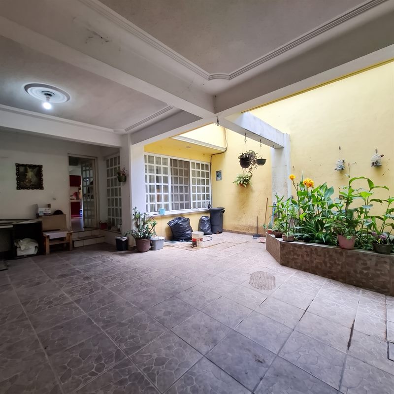 Covered tiled garage patio with raised planter of tropical plants beside the house in San Antonio de la Cal, Oaxaca