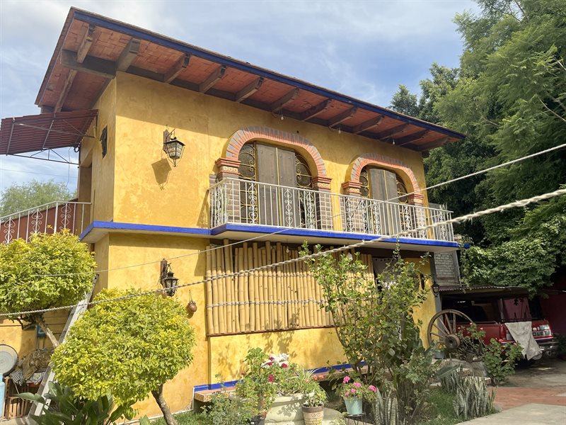 Two floor yellow apartment building with balcony and arched doorways behind the main house in El Tule